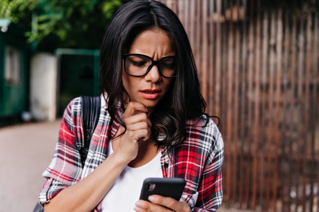 unsolicited pics anned unhappy woman glasses standing street with phone beautiful serious girl read message